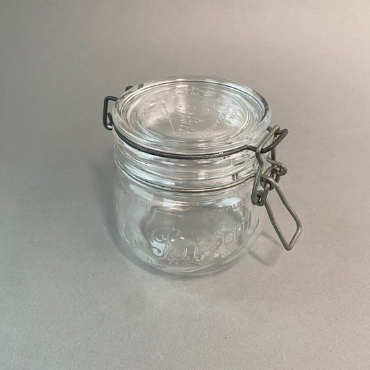 Photograph of an antique mason jar with french text. Closing mechanism has a very nice patina. 
