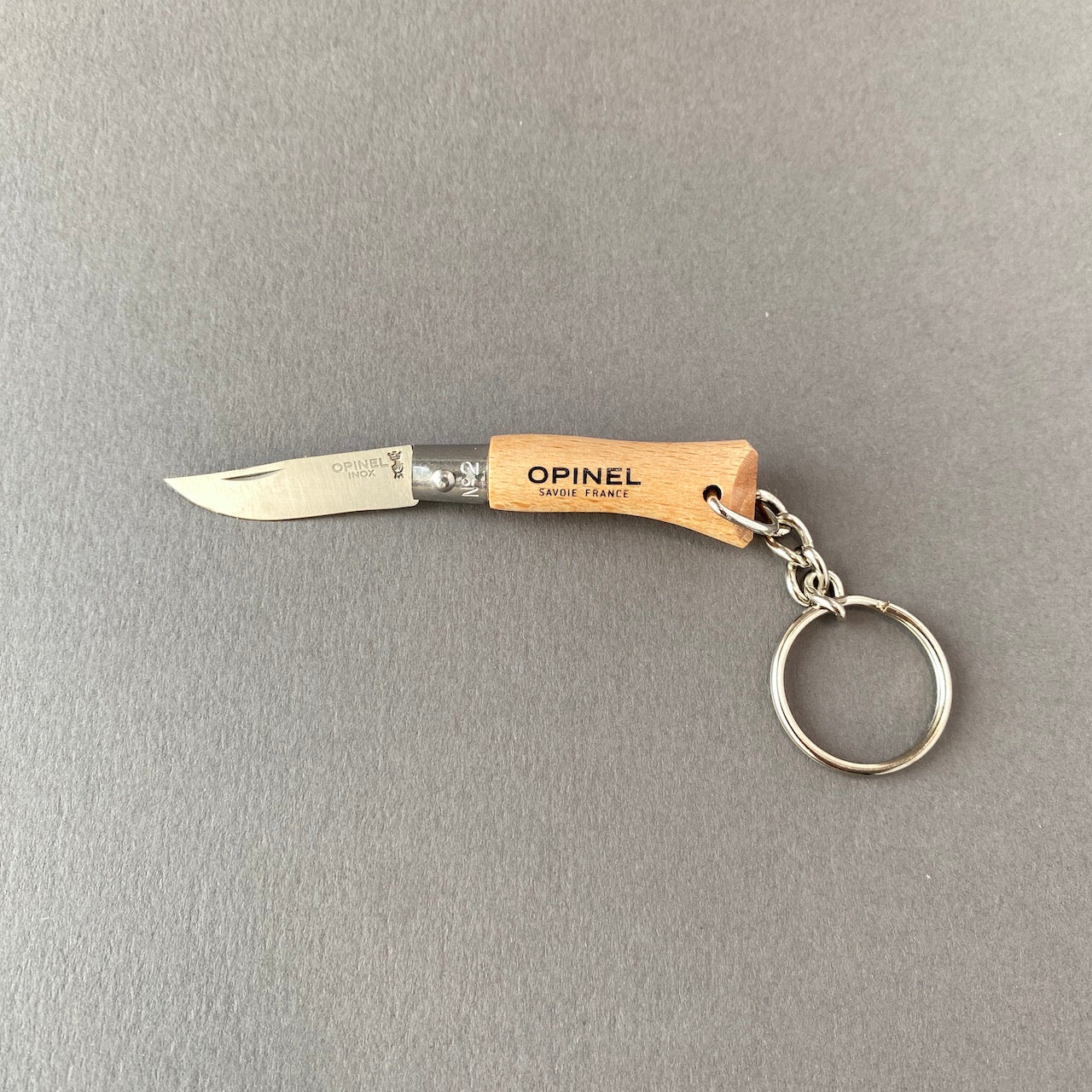 Small key chain pocket knife made out of beech wood with stainless steel blade connected to key ring with small chain-folded open