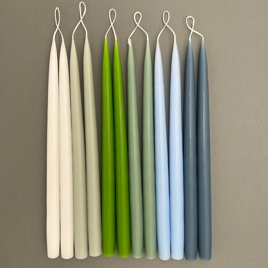 Hand dipped candles in pairs in a variety of different colors laying on a gray background