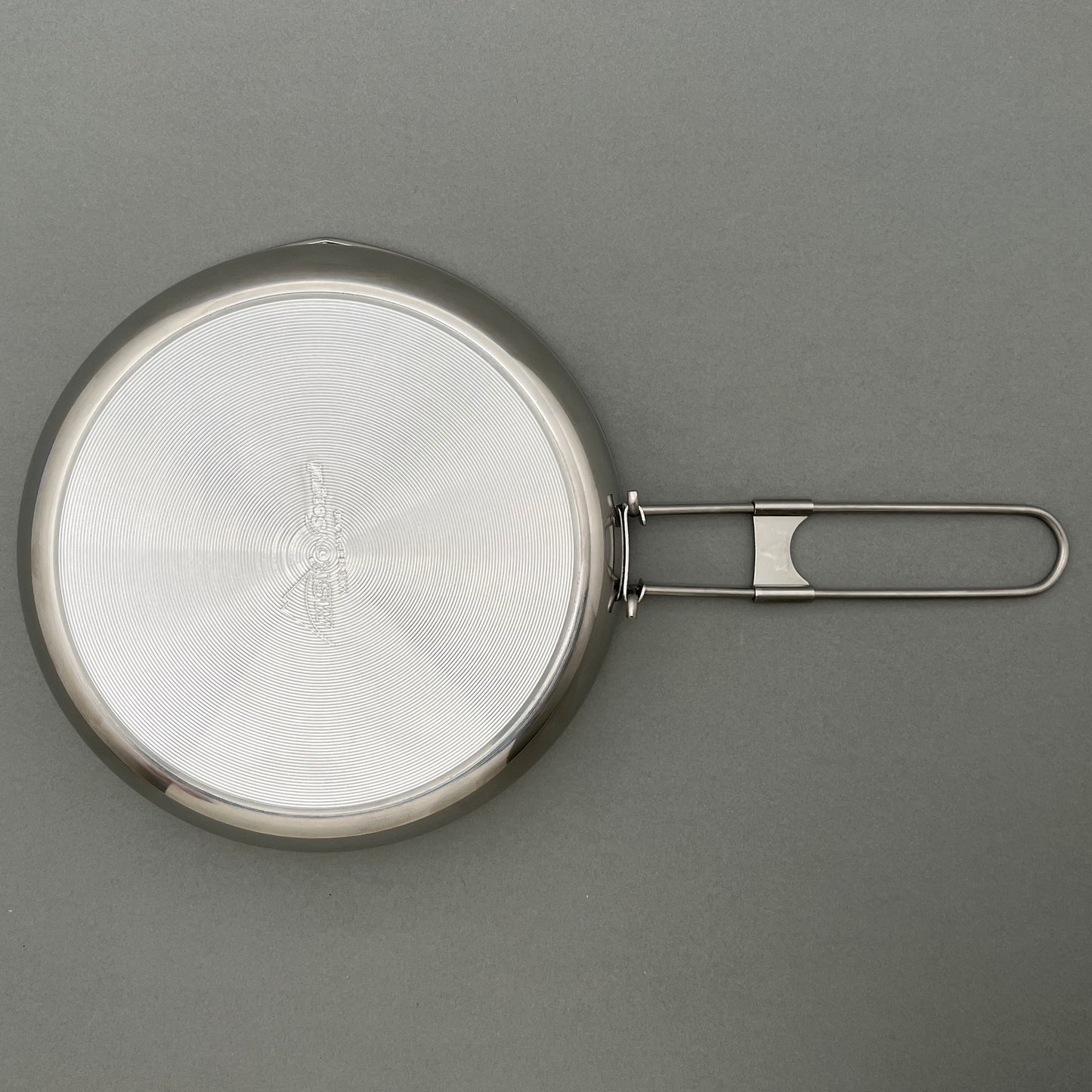 The backside of a stainless steel fry pan on a gray background