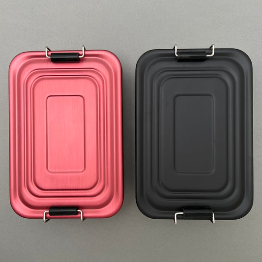 Two red and black aluminum lunchboxes laying next to each other on a grey background