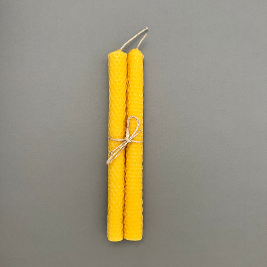 A pair of yellow candles made out of beeswax that are wrapped togheter with a piece of string laying on a grey background