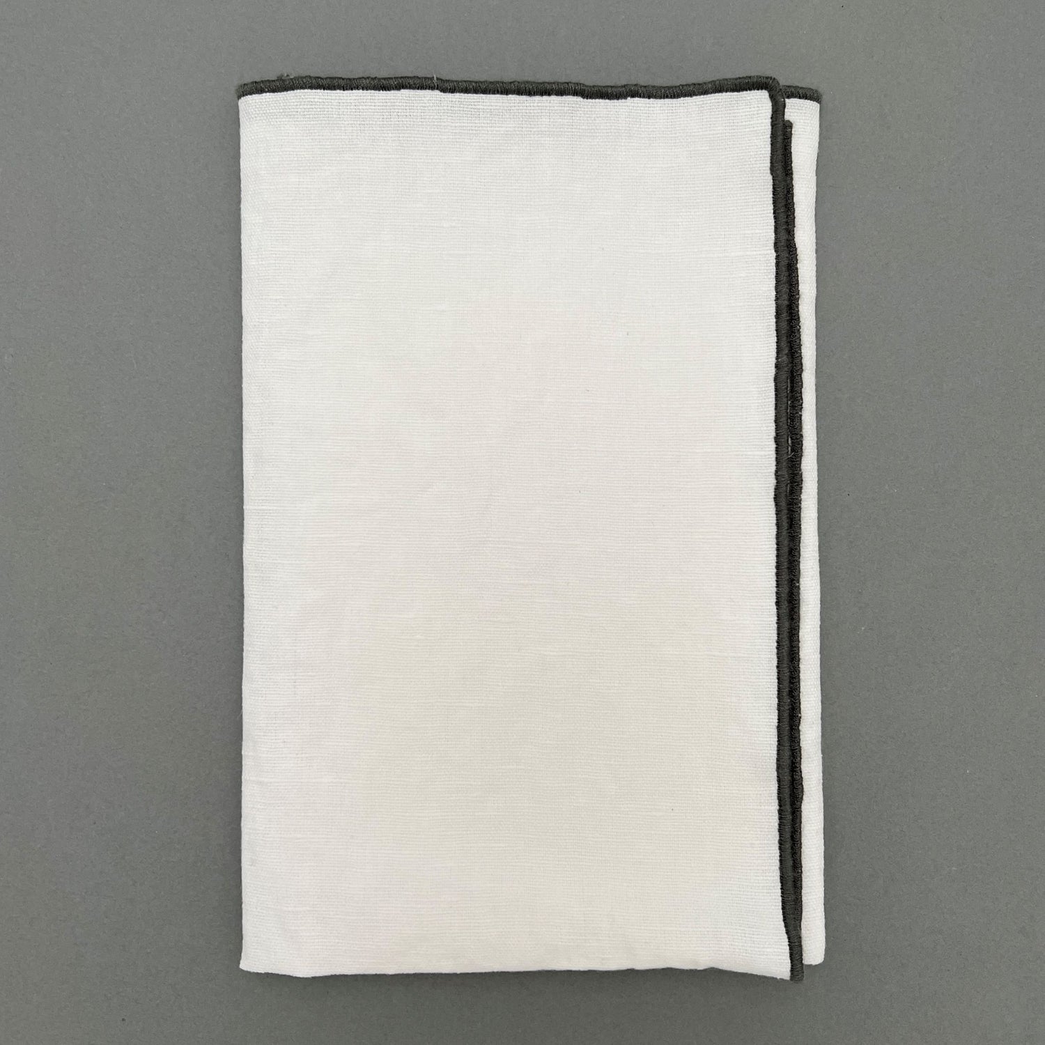 A folded white napkin with a black sewn outline laying on a gray background