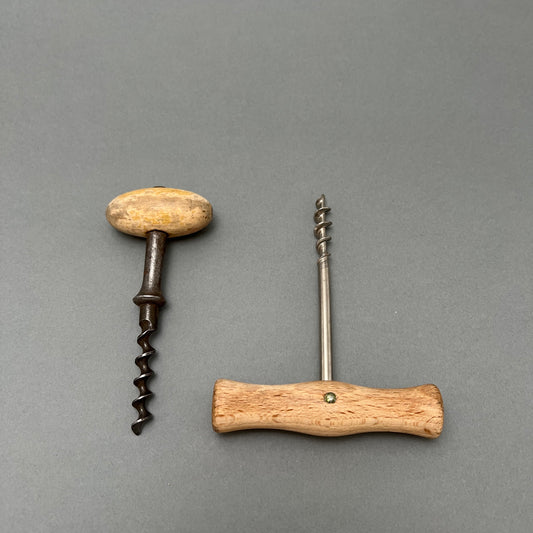 Two corkscrews with wooden handles laying next to each other on a gray background