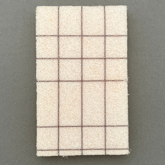 Awhite and black checkered patterned rectangular kitchen sponge laying on a gray backgrund