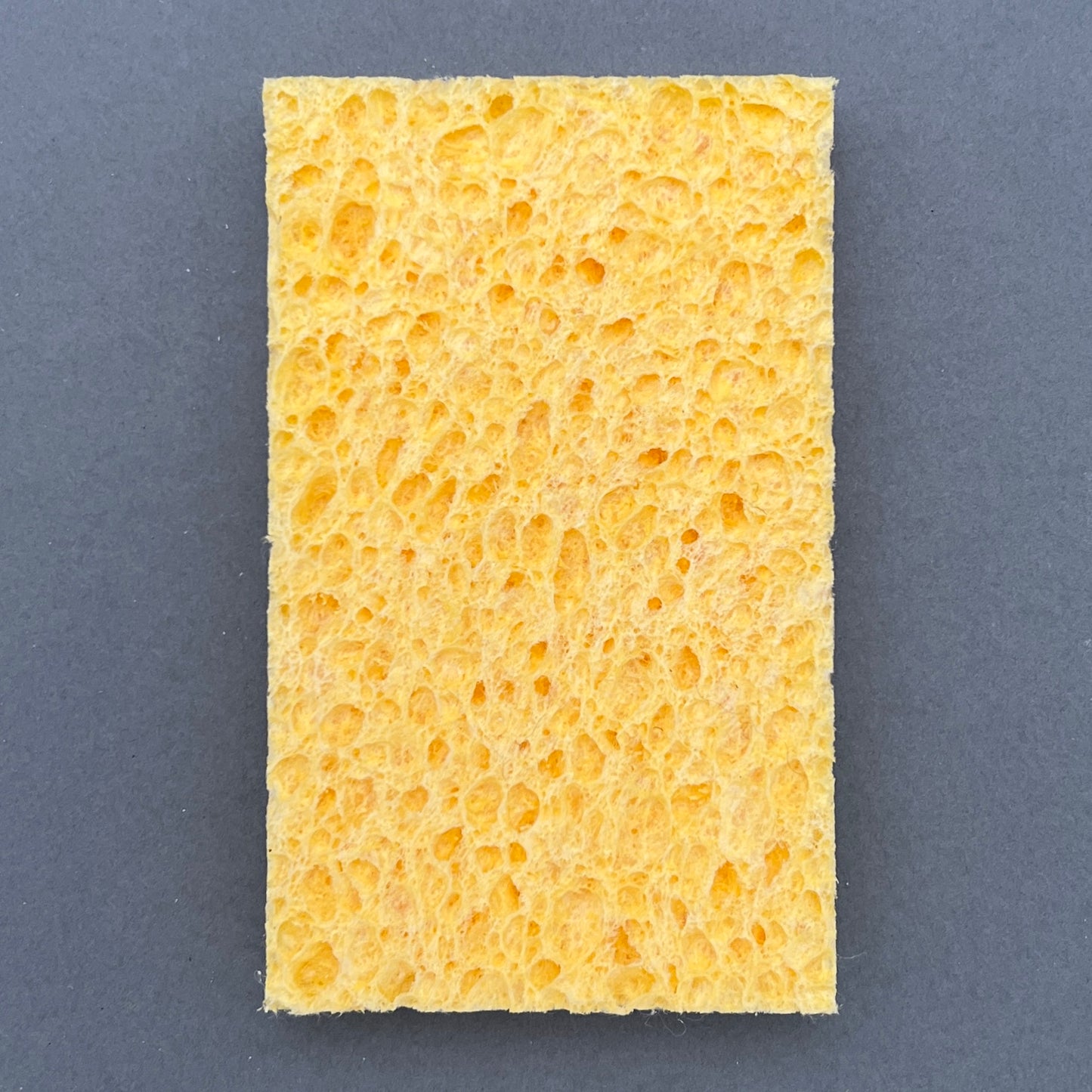 The backside of a rectangular kitchen sponge laying on a gray background