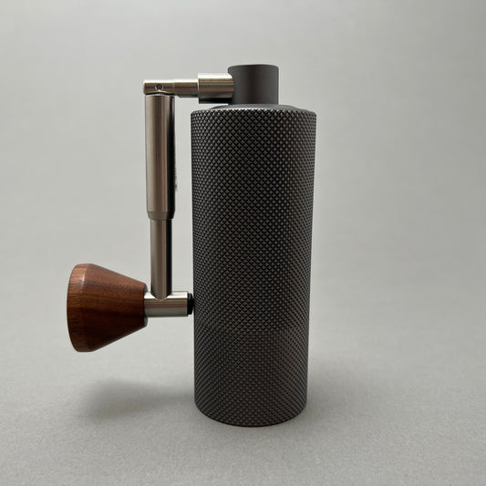 A portable steel coffee grinder with a wooden handle standing on a gray background