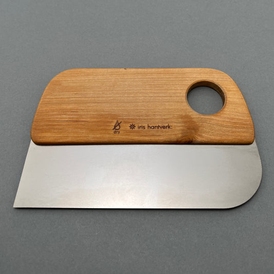 A steel dough scraper with a wooden handle with a hole cut out laying on a gray background