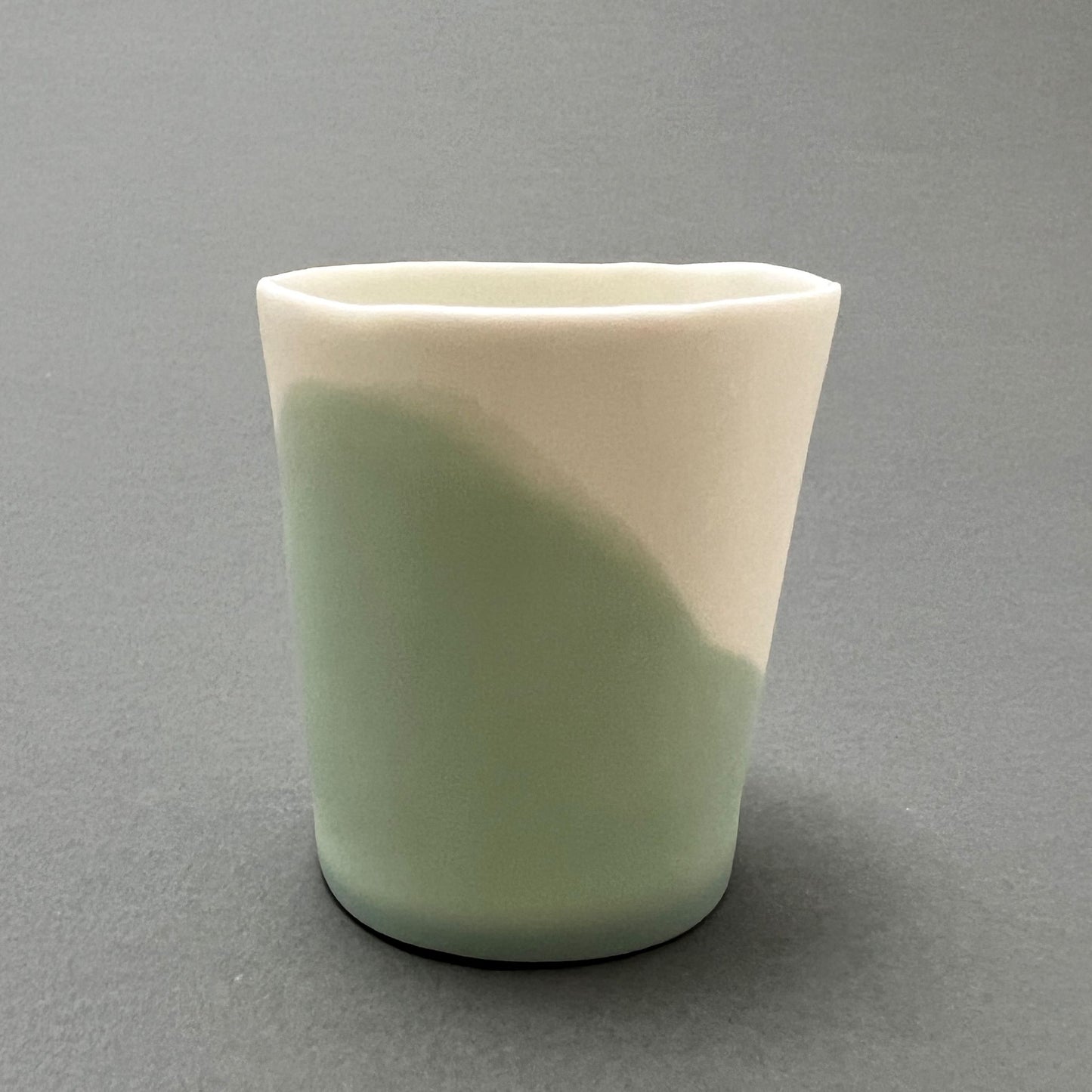 A small aqua blue and white colored porcelain cup standing on a gray background
