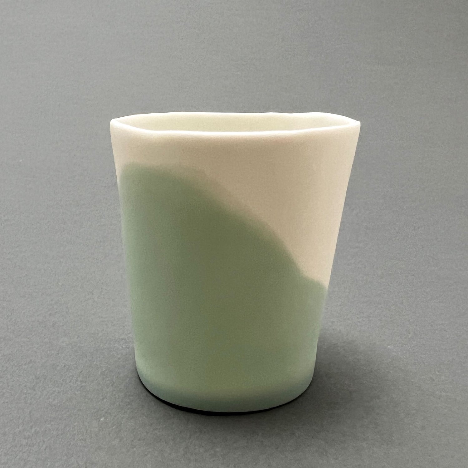 A small aqua blue and white colored porcelain cup standing on a gray background