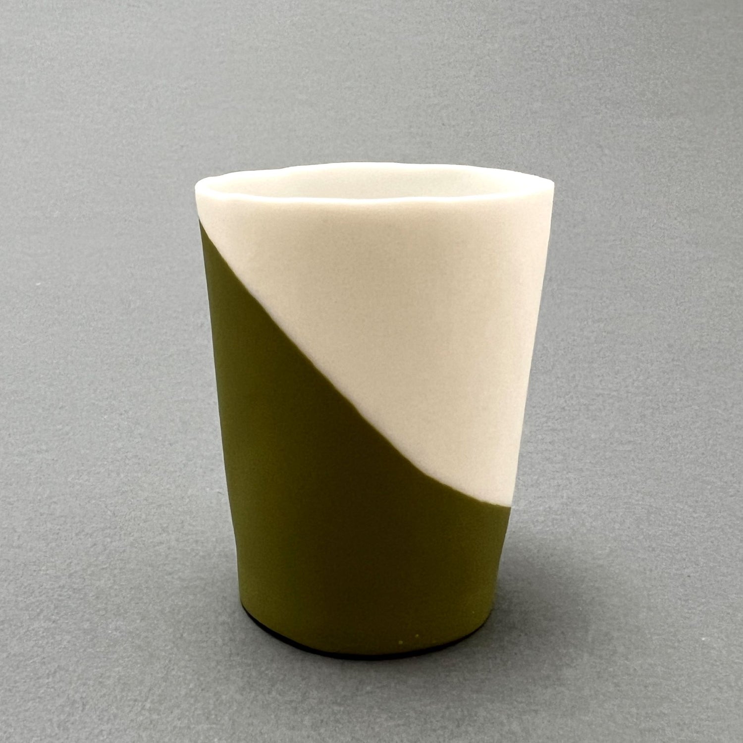 A small forest green and white colored porcelain cup standing on a gray background