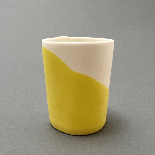 A small yellow and white colored porcelain cup standing on a gray background