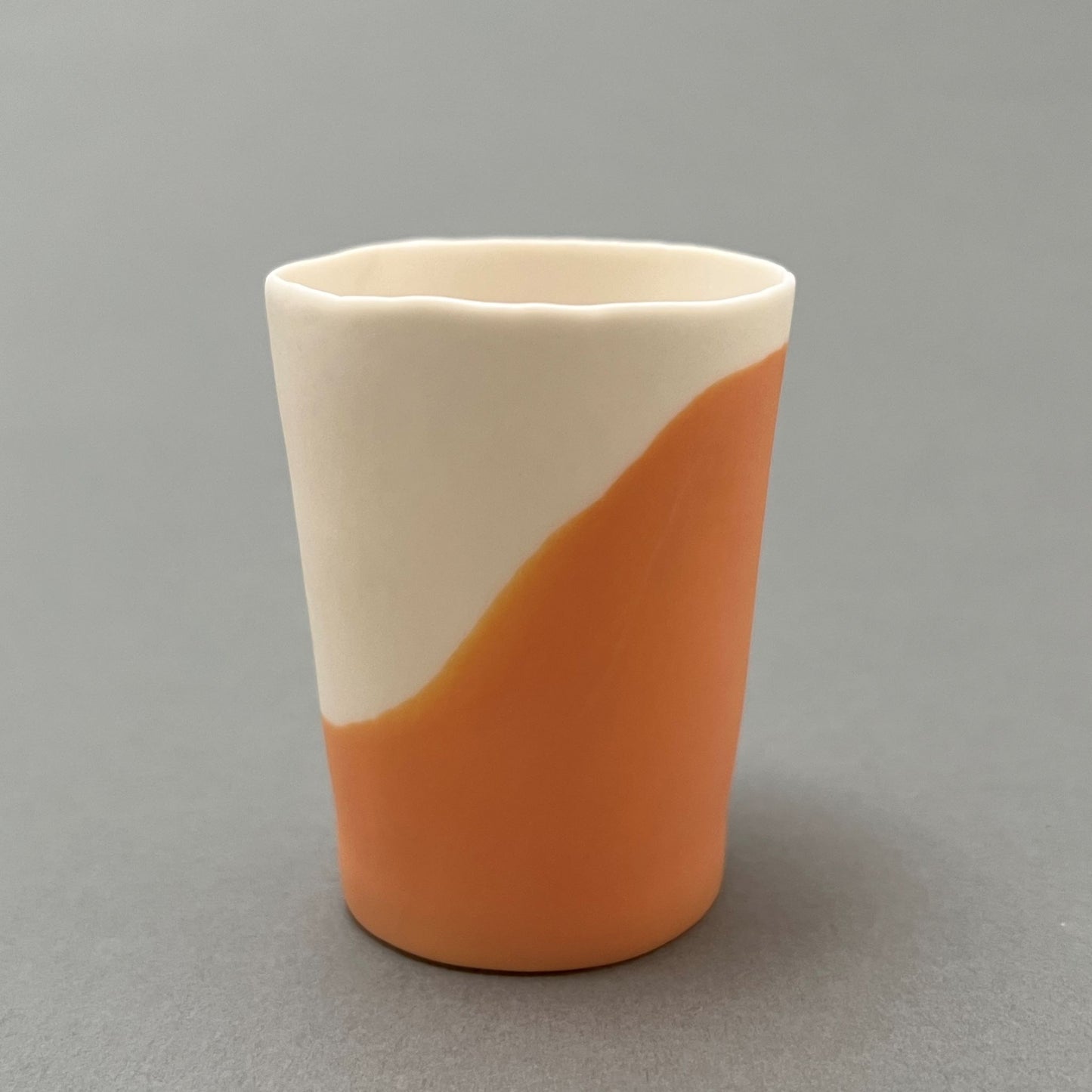 A small orange and white colored porcelain cup standing on a gray background