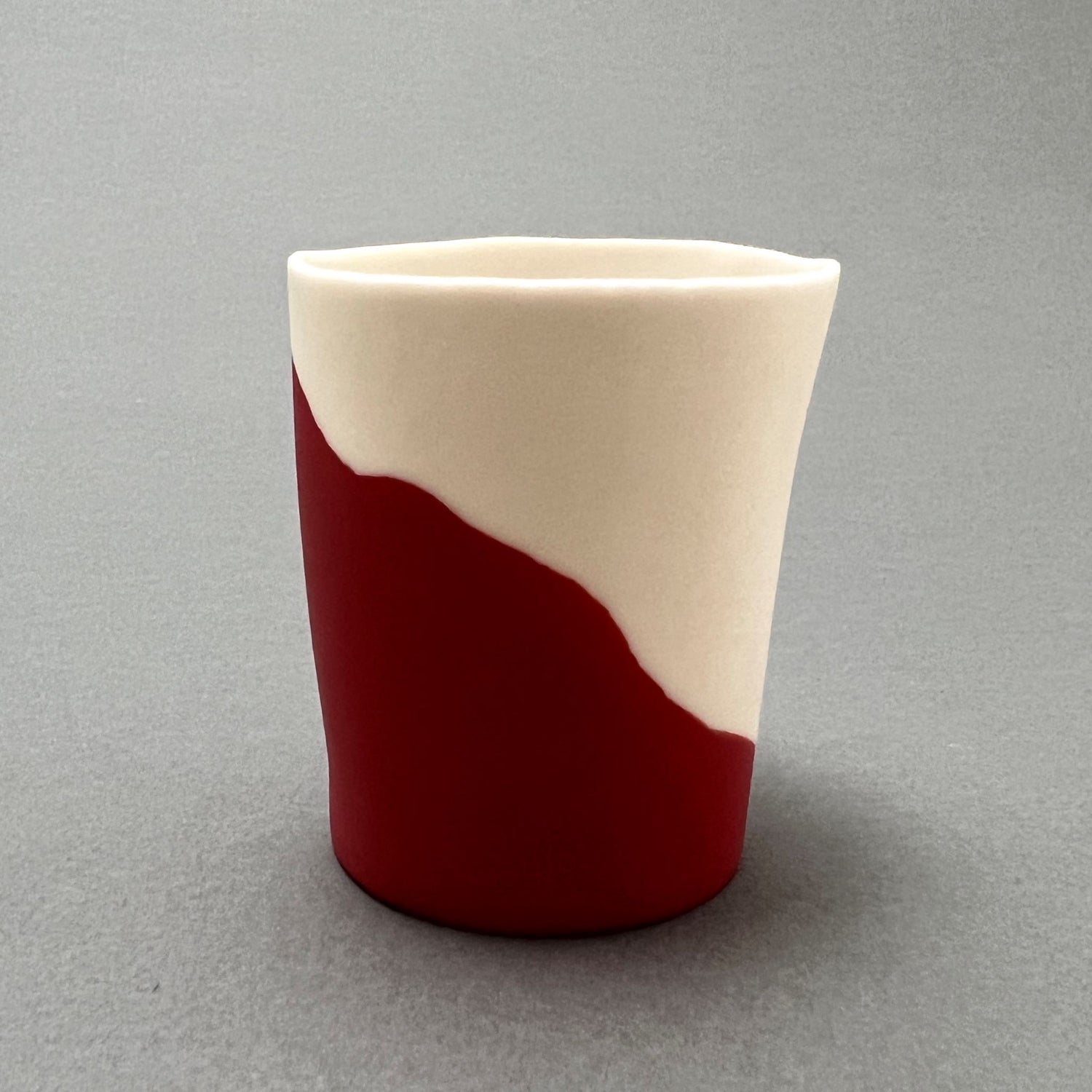 A small red and white colored porcelain cup standing on a gray background