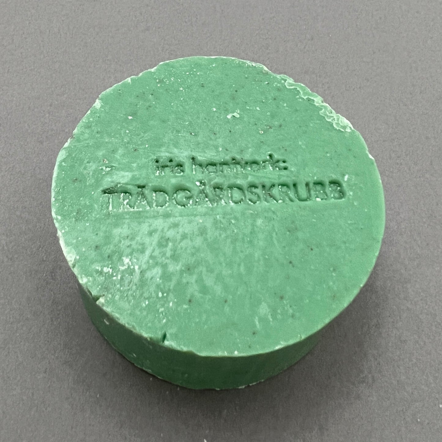 A round green handmade garden soap from iris hanteverk laying on a gray background