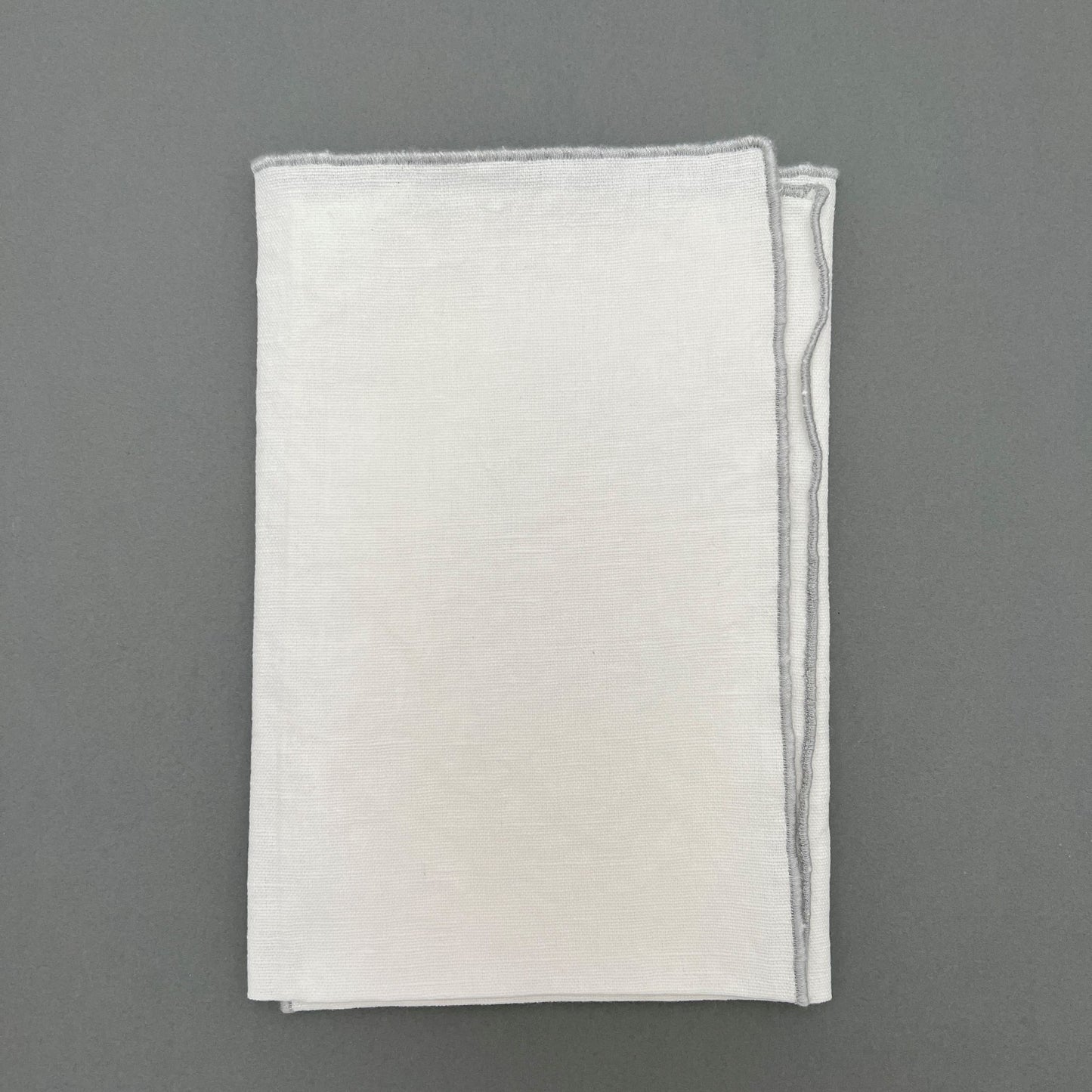 A folded white napkin with a gray sewn outline laying on a gray background
