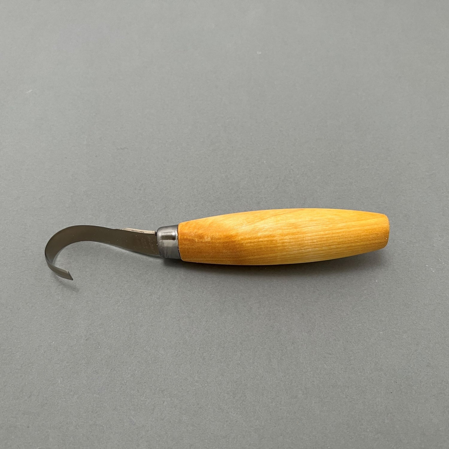 A steel hook knife with a wooden handle laying on a gray background