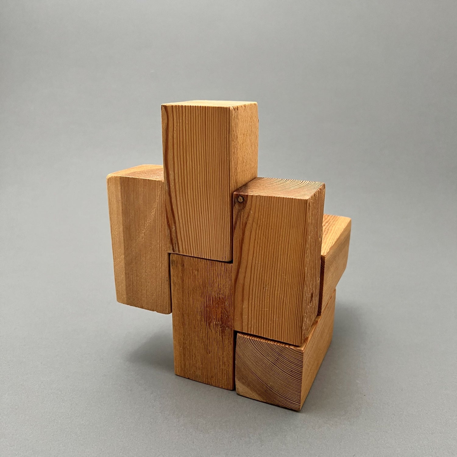 A kinectic sculpture made out of rectangular wooden pieces sitting on a gray background