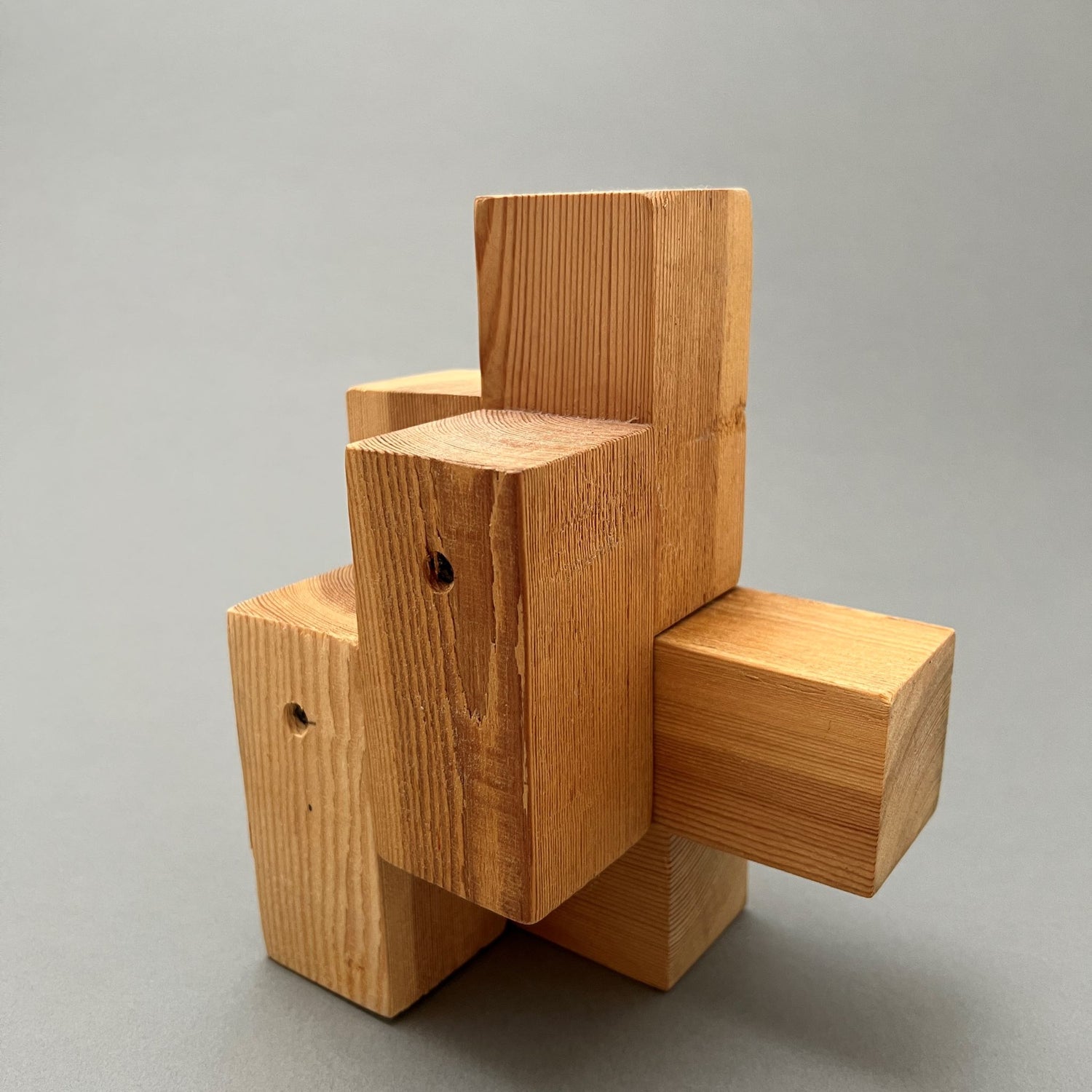 A kinectic sculpture made out of rectangular wooden pieces sitting on a gray background
