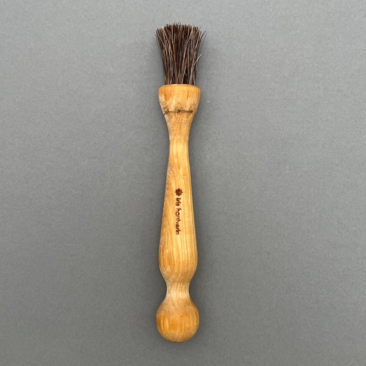 A mushroom brush made with oiled birch and horsehair laying on a gray background