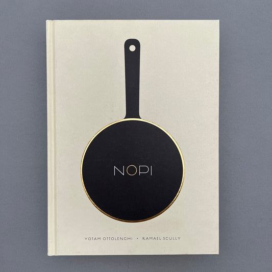 A white colored book called NOPI with a picture of a fry pan on the cover. The book is laying on a gray background