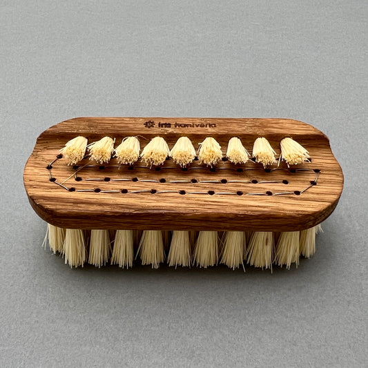 A Double-sided nail brush made out of oil treated oak and tampico fibre laying on a gray background