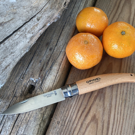 A stainless steel folding knife from Opinel with a wooden handle laying next to three clementines on rough sawn wood