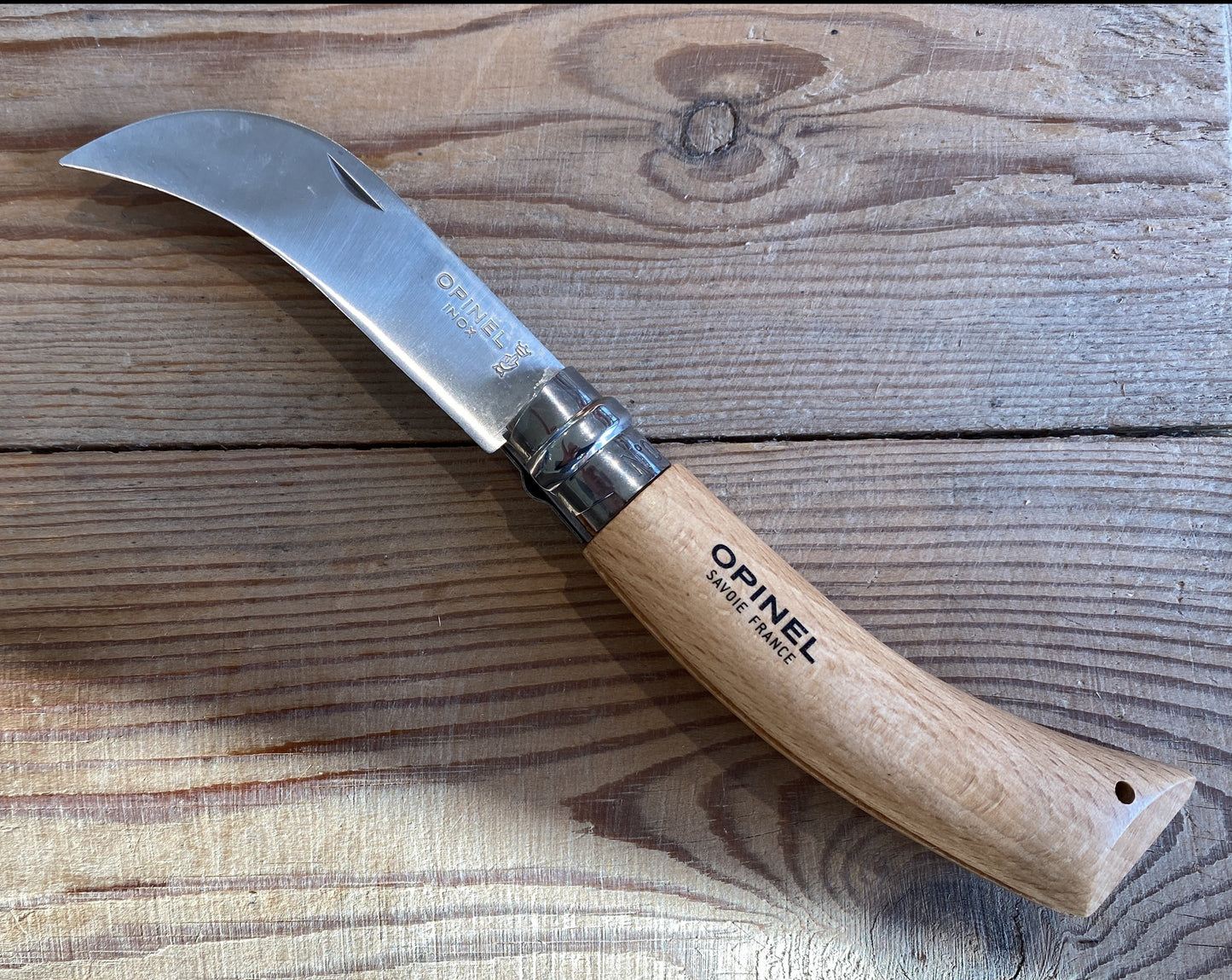A stainless steel pruning folding knife from Opinel with a wooden handle laying on a wooden table