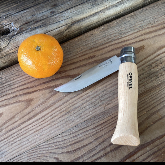 A stainless steel folding knife from Opinel with a wooden handle laying next to a clementine on rough sawn wood