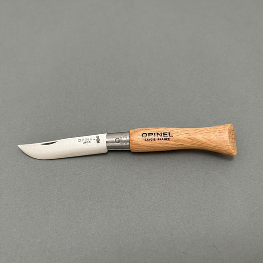 A stainless steel folding knife from Opinel with a wooden handle laying on a gray background