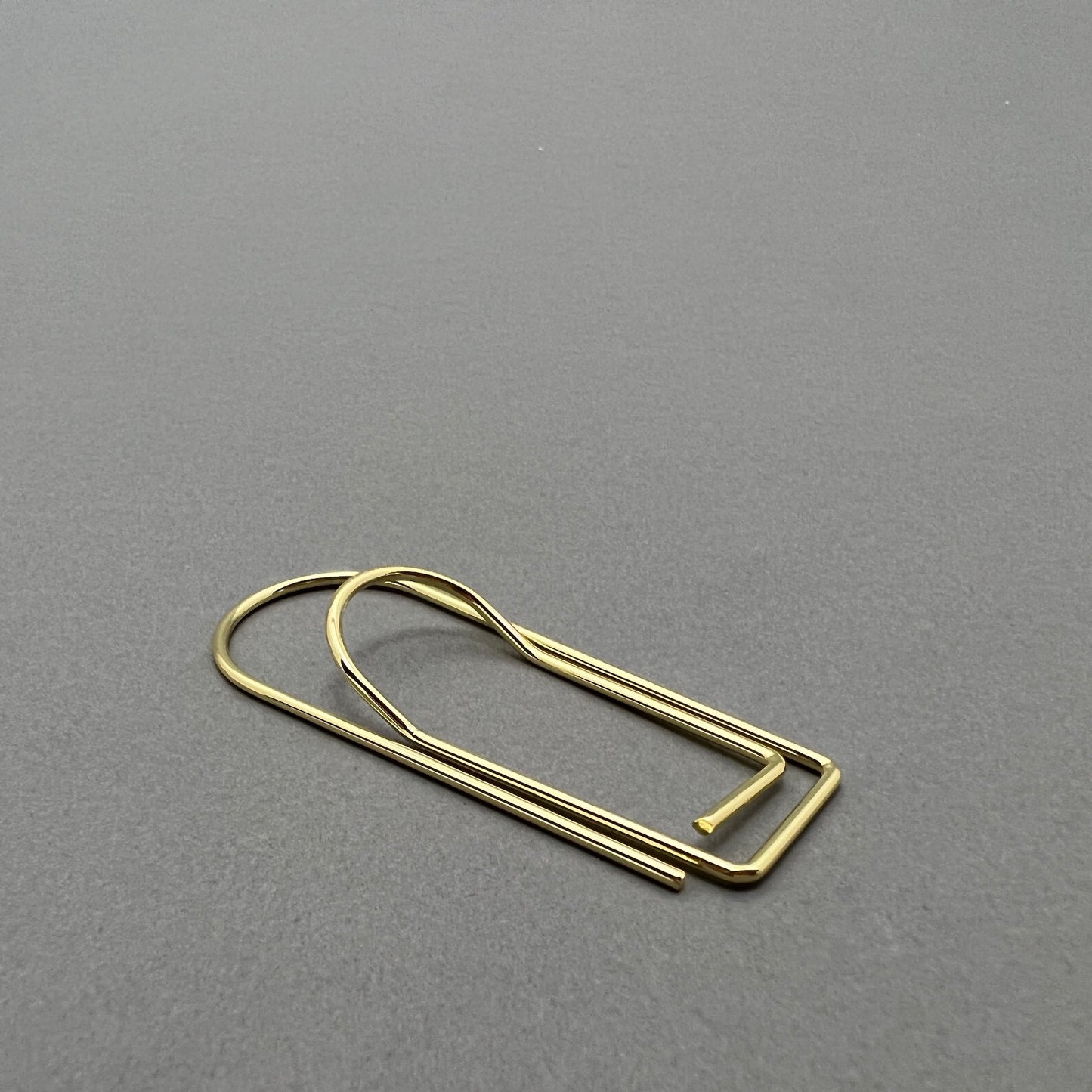 A gold colored iron paper clip laying on a gray background