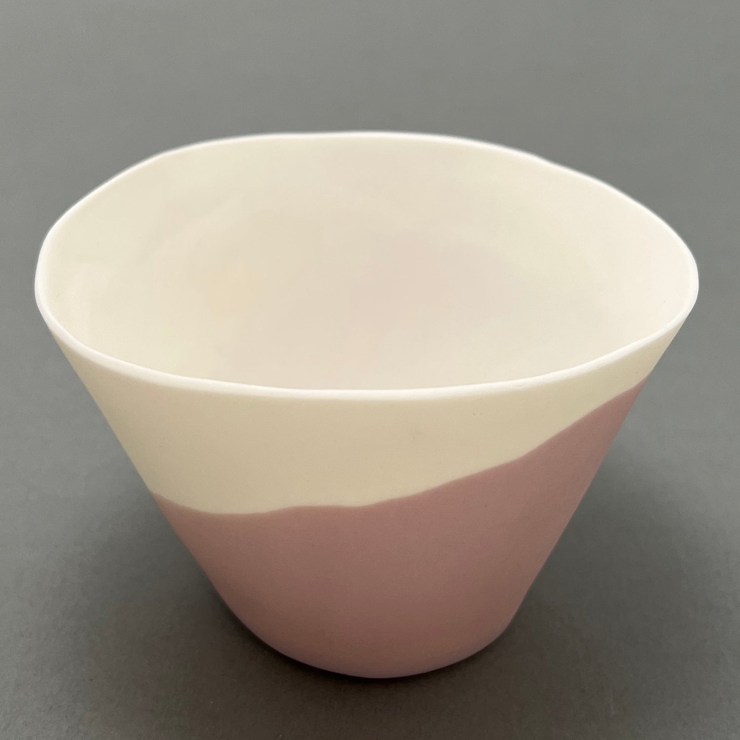 A white and pink coloured porcelain bowl standing on a gray background