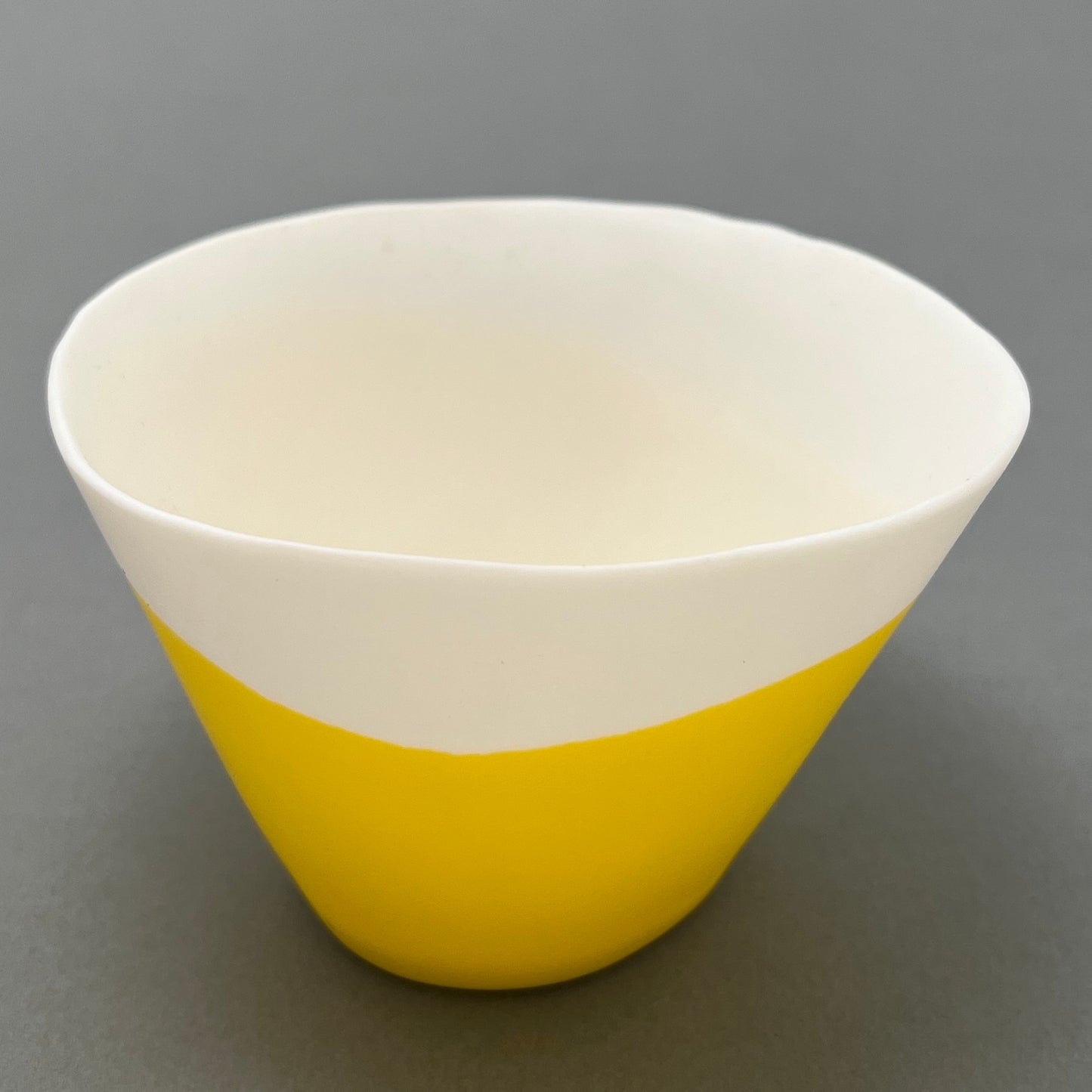 A white and yellow coloured porcelain bowl standing on a gray background 