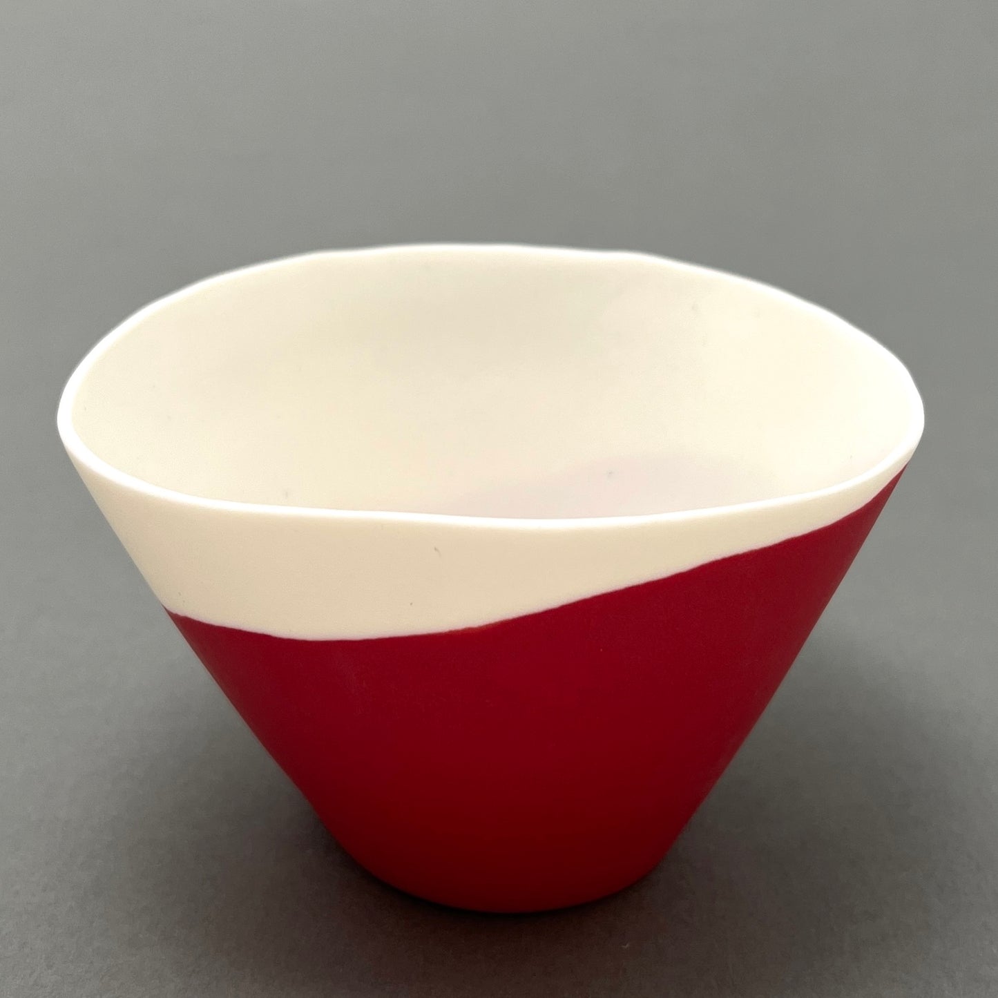 A white and red coloured porcelain bowl standing on a gray background