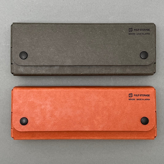 A black and orange pen case made in japan laying next to each other on a gray background
