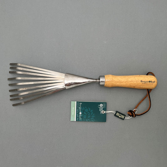 Burgon&Ball shrub rake made of steel with a wooden handle laying on a gray background