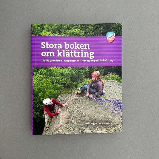 A purple colored book called "Stora boken om klättring" with a picture of two people climbing a mountain on the cover. Laying on a gray background