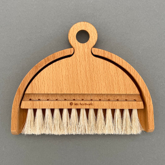 A wooden brush and shovel made out of oiled beech and horse hair laying on a gray background