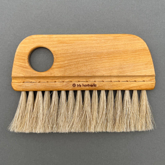A bakers brush made out of horse hair with a wooden handle laying on a gray background