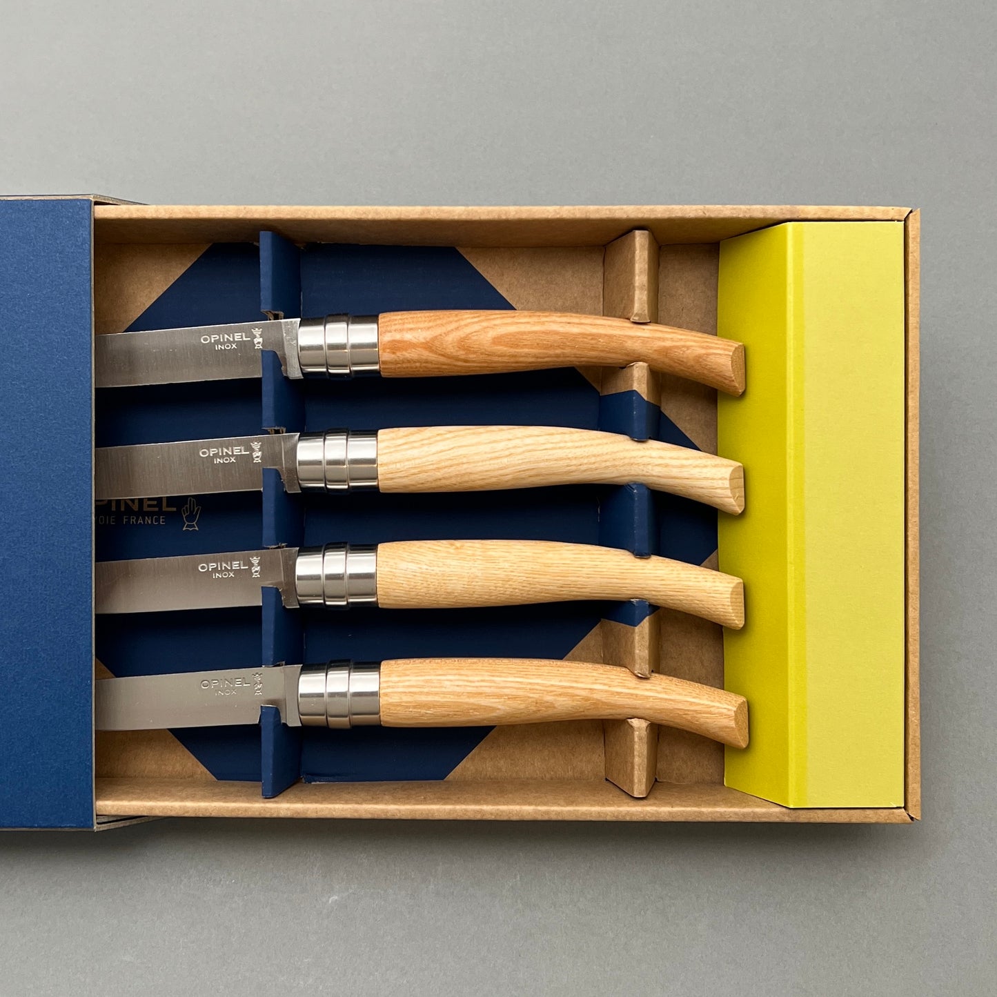 Four table knifes laying next to each other in a cardboard box on a grey background