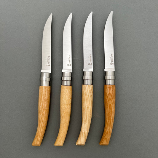 Four table knifes with wooden handle laying next to each other on a grey background
