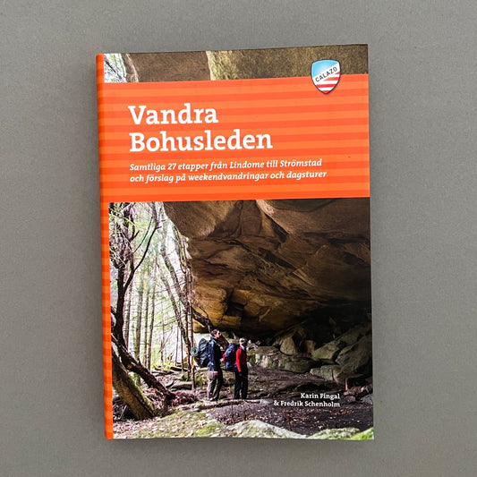 An orange colored book called "Vandra Bohusleden" with a picture of two people standing underneath a mountain on the cover