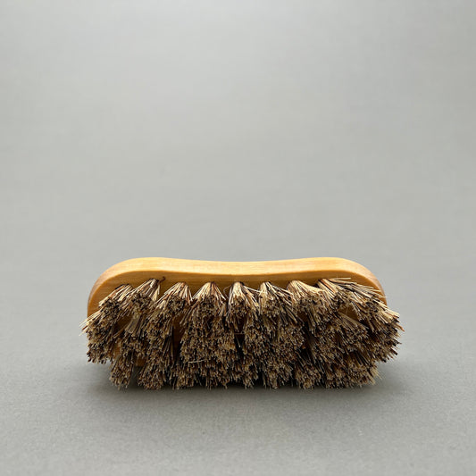 A handmade vegetable brush with a wooden handle laying on a gray background