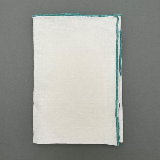 A folded white napkin with a green sewn outline laying on a gray background