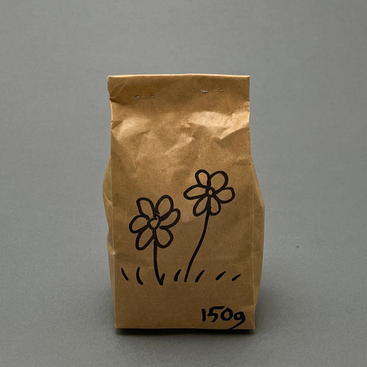 A brown paper bag filled with 150 grams of wild grass and flower mix sitting on a gray background