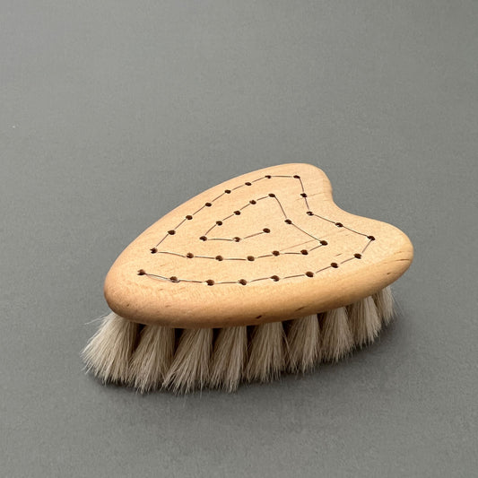 A handmade heart-shaped baby brush with a wooden handle laying on a gray background