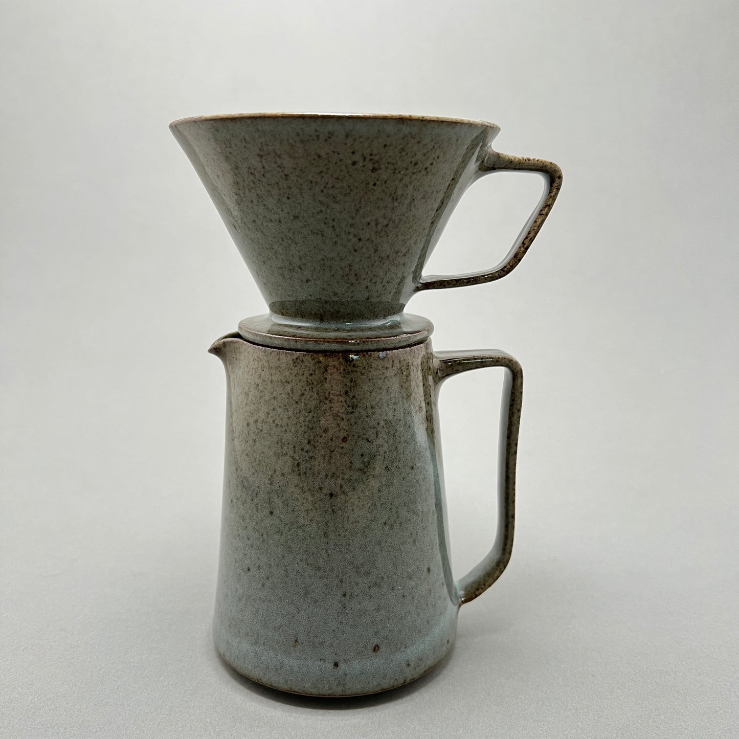 A sage green ceramic coffee pitcher standing on a gray background