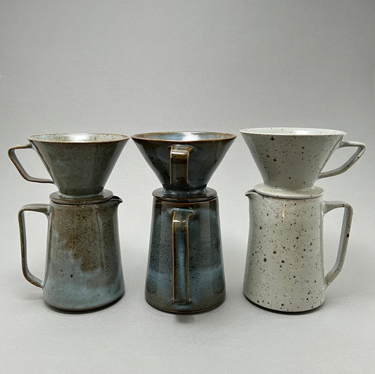 Three ceramic coffee pitchers in a variety of colors standing next to each other on a gray background
