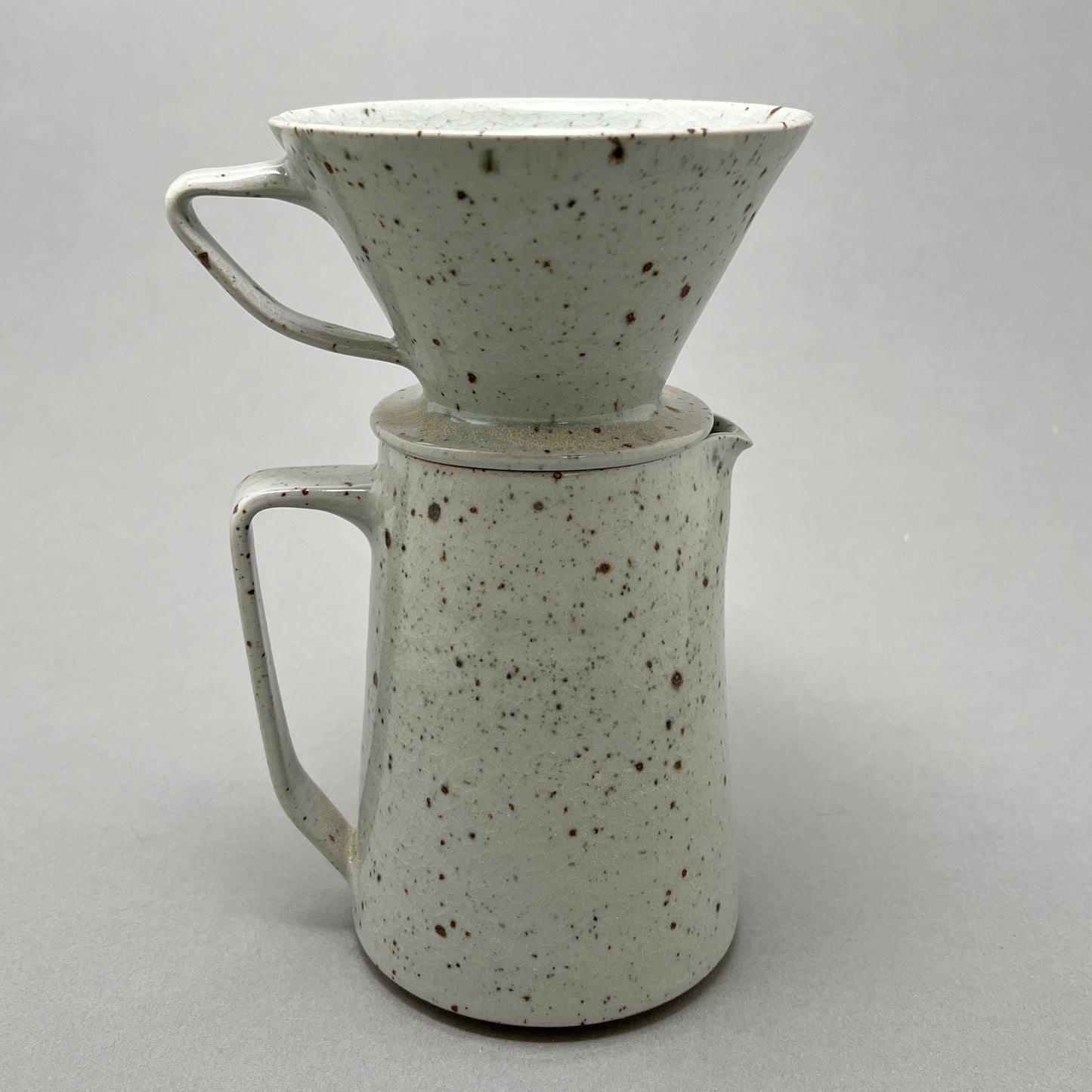 A light grey ceramic coffee pitcher standing on a gray background