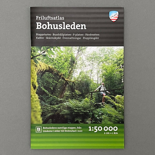 A black and green book called "Bohusleden" with a picture of a guy walking in the forest on the cover. The book is laying on a gray background 